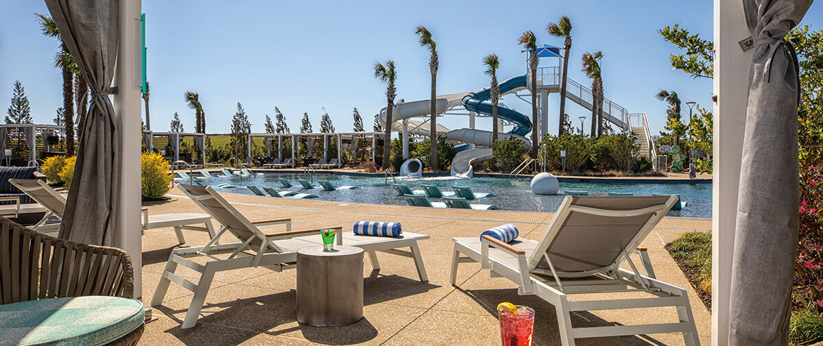 Resort pool with in-water loungers, palm trees, and a tall twisting waterslide; drinks on a small side table.
