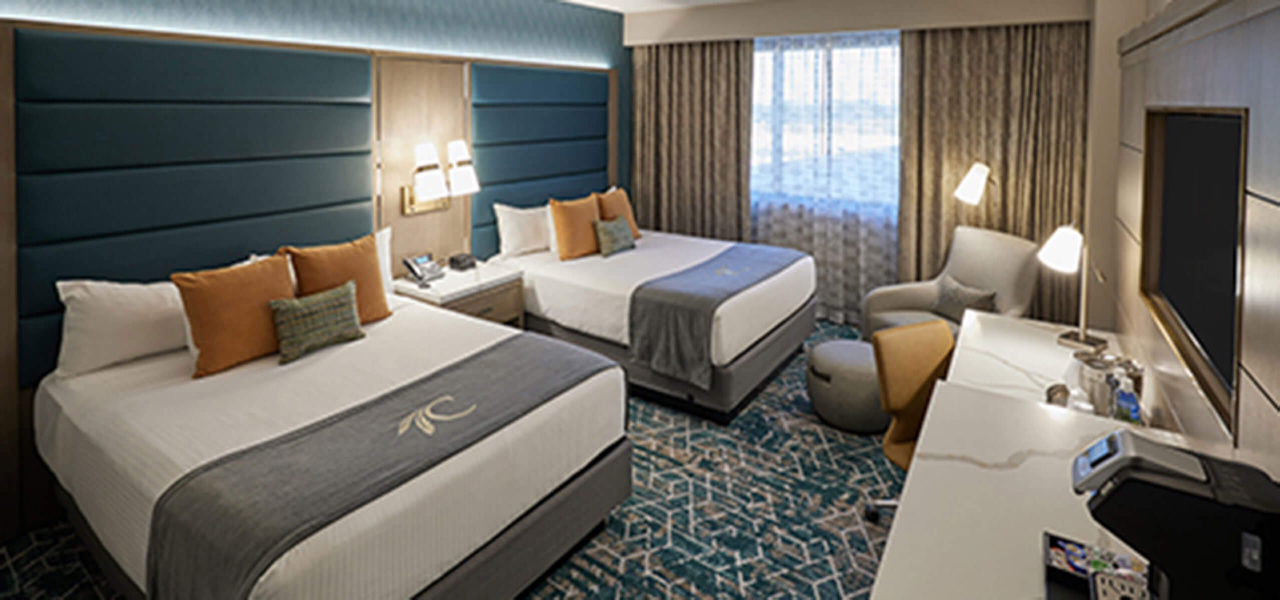 Grand Tower guest room with two queen beds, teal upholstered headboards, and a patterned carpet.