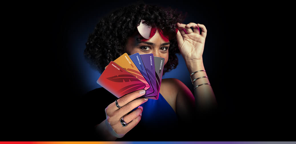 Woman lifting sunglasses while fanning out colorful casino rewards cards against a dark background