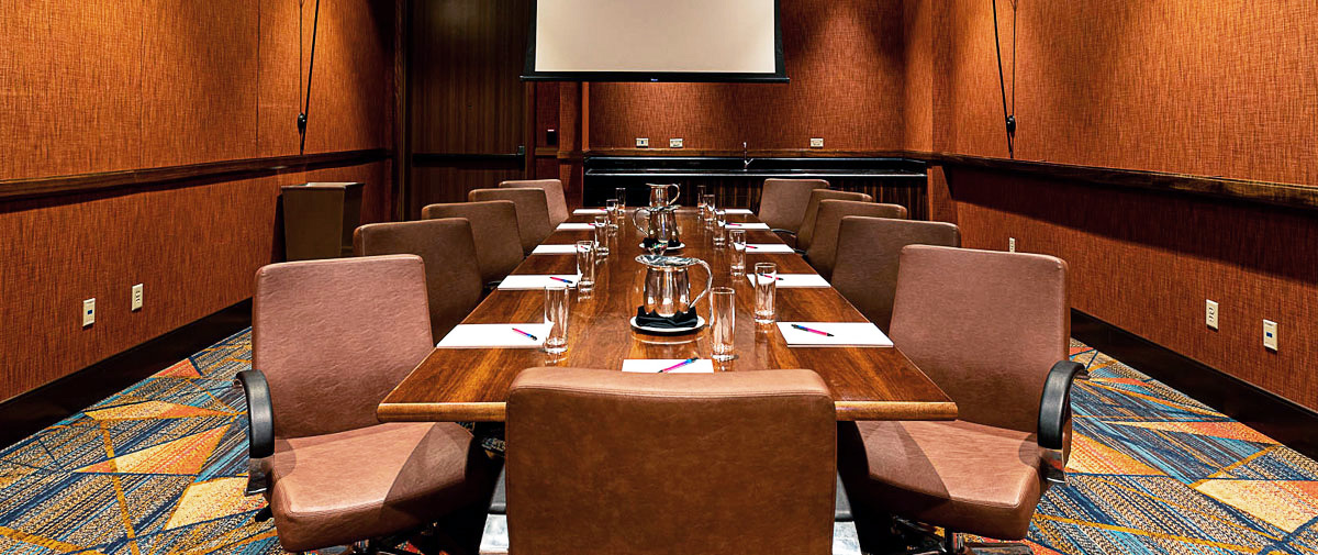 Alternate view of the Cypress Boardroom—long table set with notepads, leather chairs, and warm ambient lighting