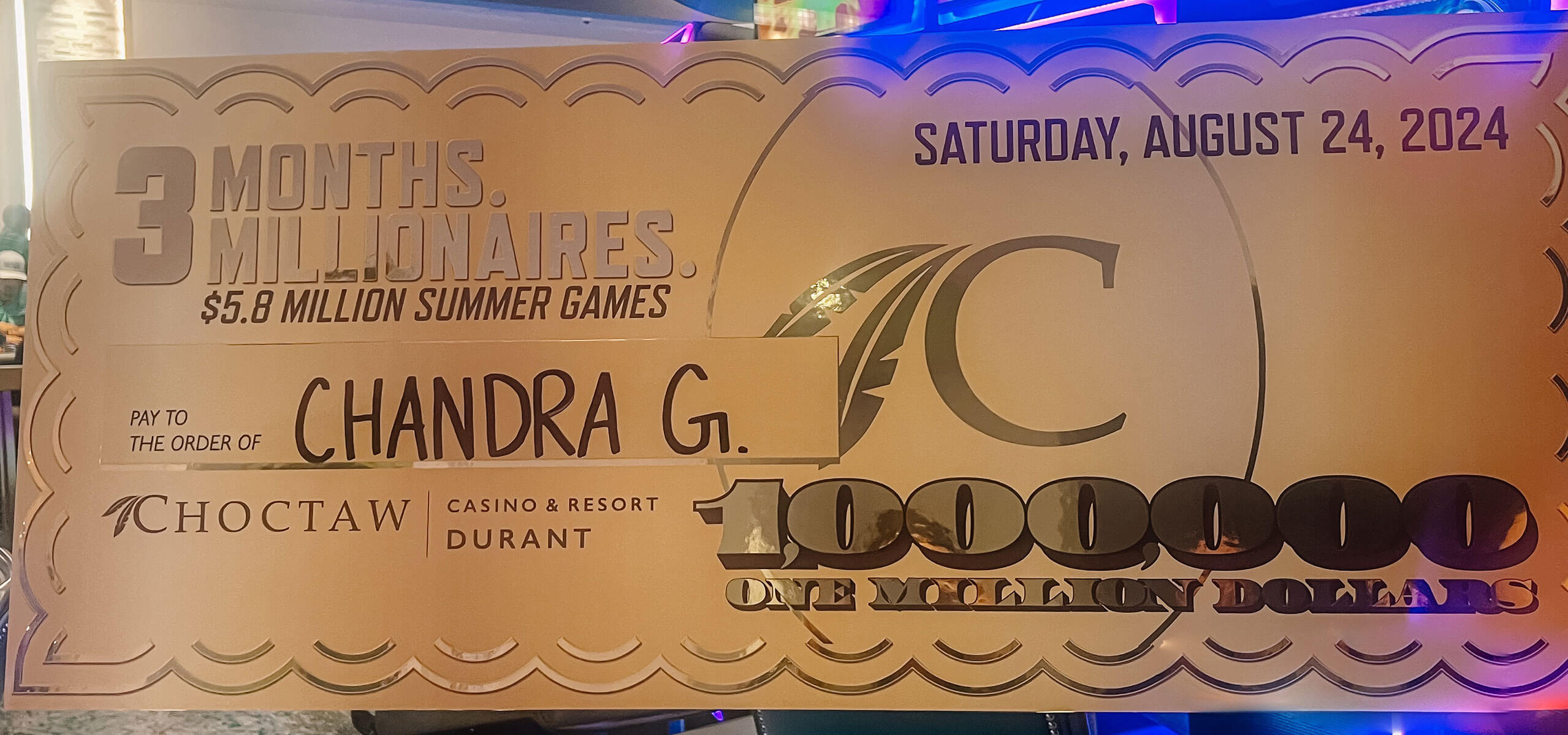Oversized ceremonial check reading ‘3 MONTHS. 3 MILLIONAIRES. $5.8 MILLION SUMMER GAMES,’ made out to ‘Chandra G.’ for ONE MILLION DOLLARS